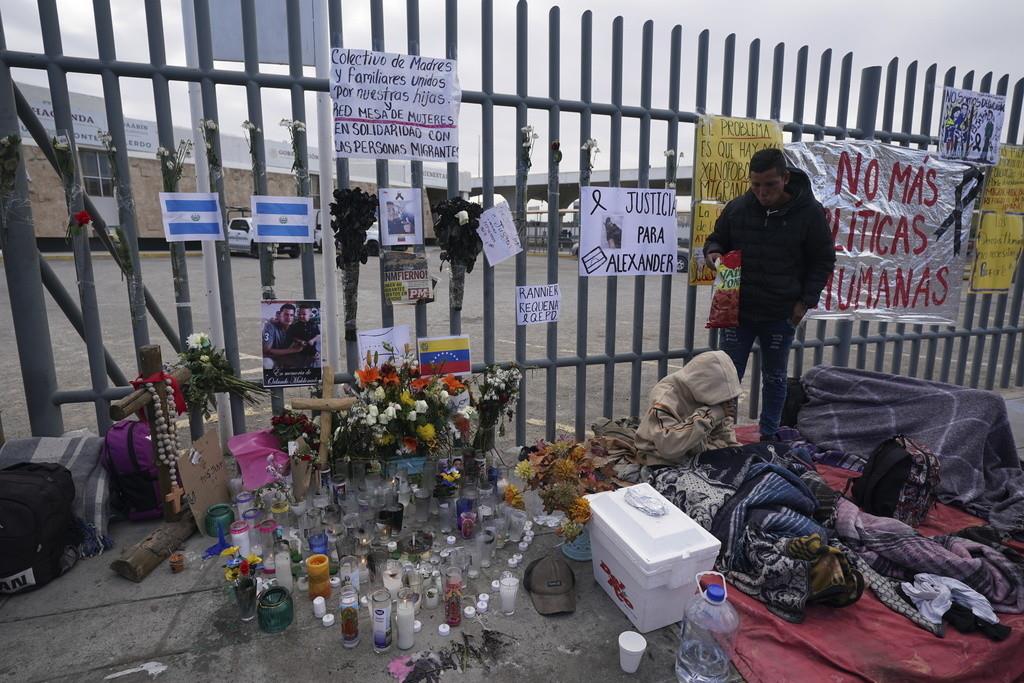 Un altar con velas y fotos cubre la cerca afuera del centro de detención de migrantes que fue el sitio de un incendio mortal, mientras los migrantes se despiertan después de pasar la noche en la acera en Ciudad Juárez, México, el jueves 30 de marzo de 2023