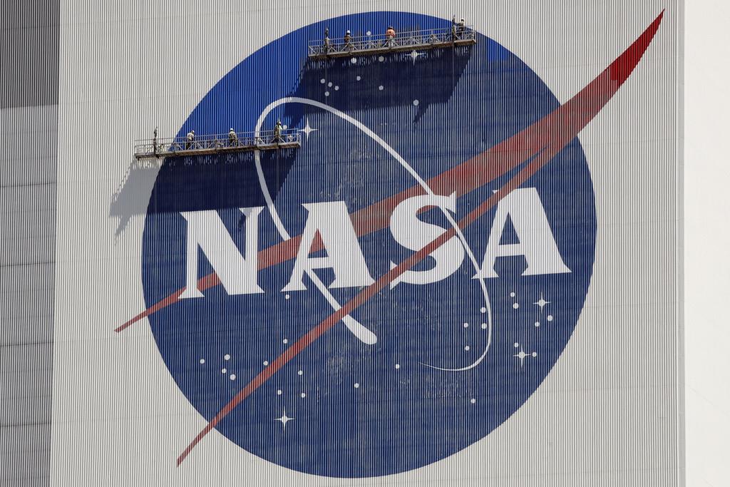 Trabajadores en andamios repintan el logotipo de la NASA en una pared del edificio de ensamblaje de vehículos espaciales en el Centro Espacial Kennedy el 20 de mayo de 2020, en Cabo Cañaveral, Florida. (AP Foto/John Raoux, Archivo)