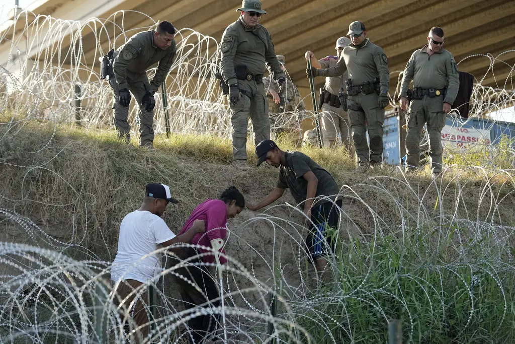 Soldados y guardias de Texas ayudan a una migrante que quedó atrapada en un alambre de púas después de cruzar el Río Grande desde México hacia EEUU, el 1 de agosto de 2023, en Eagle Pass, Texas. (Foto AP/Eric Gay)