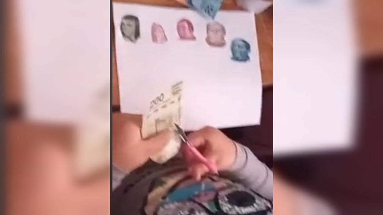 Niña recorta billetes de diferentes denominaciones para su tarea. Foto. Captura de Imagen