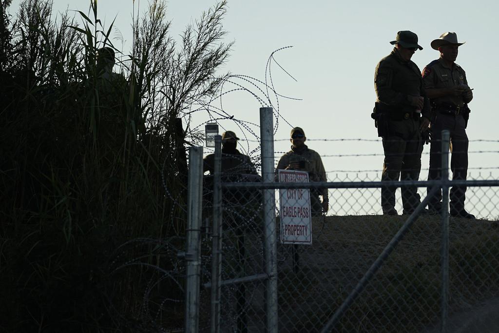 Policías estatales de Texas vigilan junto a un letrero de Prohibido el paso y alambre de púas a lo largo de las márgenes del río Bravo (o Grande), el 1 de agosto de 2023, en Shelby Park, Eagle Pass, Texas. (AP Foto/Eric Gay, Archivo)