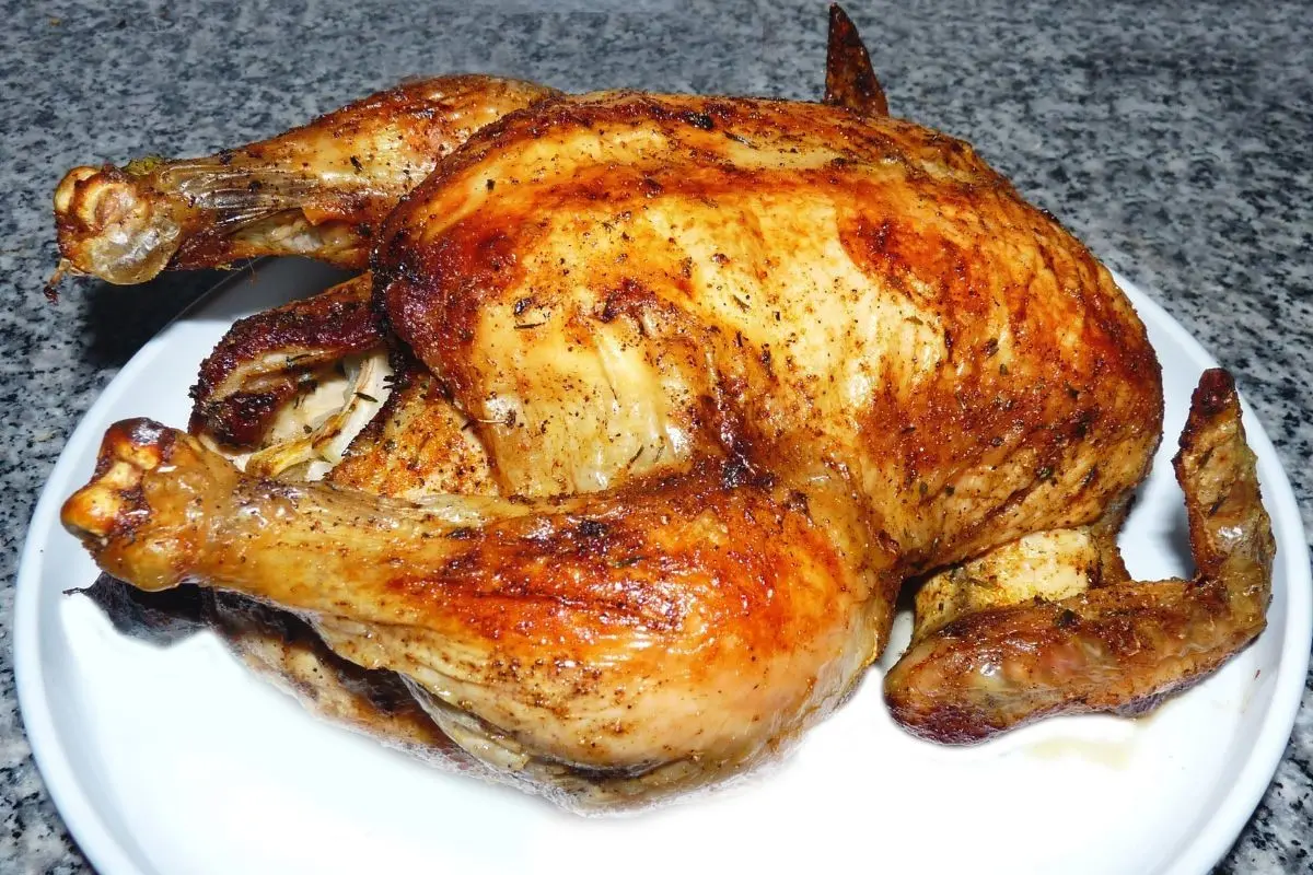 Un pollo asado con condimentos sobre un plato color blanco: Canva