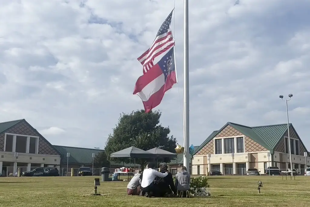 Un grupo de personas se reúne en el asta de la bandera frente a la entrada de la escuela secundaria Apalachee, el jueves 5 de septiembre de 2024 en Winder, Georgia, un día después del tiroteo en la escuela. (AP Foto/Sharon Johnson)