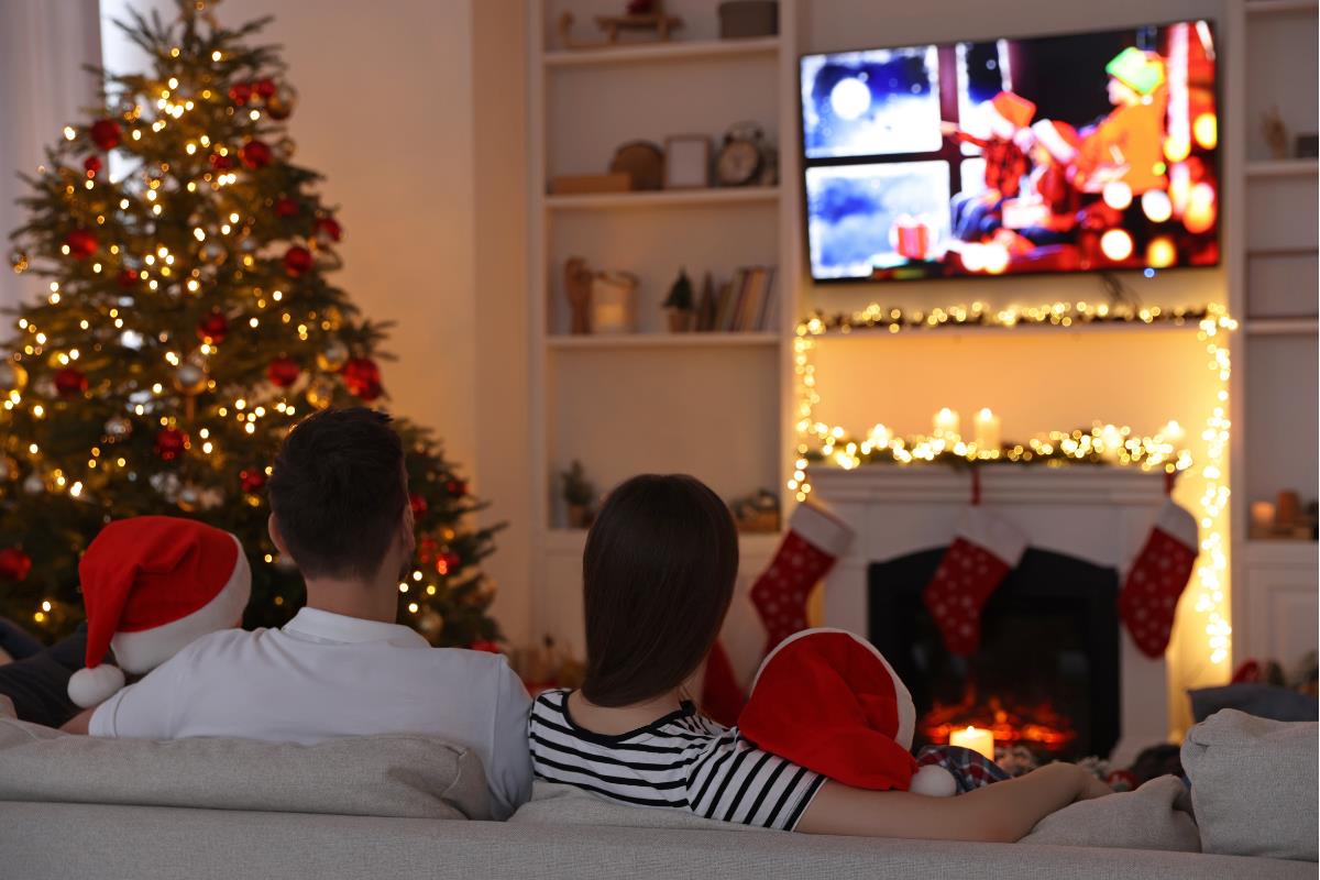 Personas viendo la televisión en cuarto navideño. Foto: Canva