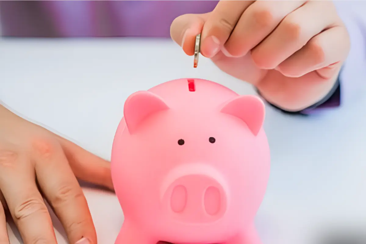 Persona metiendo una moneda a una alcancía de puerquito para ahorrar. Foto: Freepik, redimensionada en Canva.