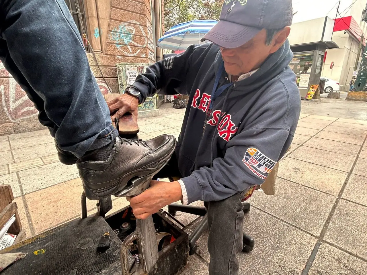 Sergio Pérez Castillo lustrador de zapatos atendiendo a un cliente. Foto: Rosy Sandoval.