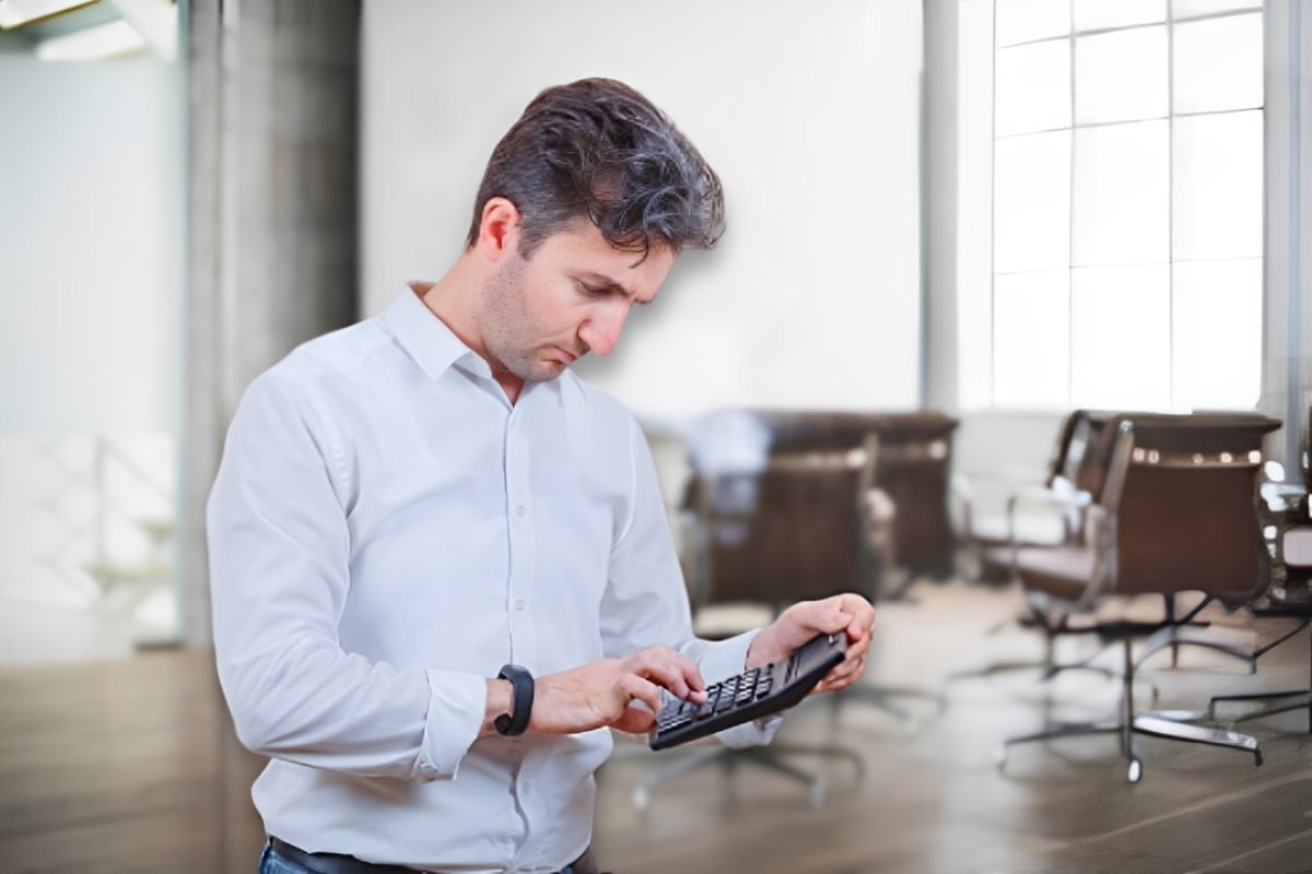 Hombre sosteniendo una calculadora para el cálculo de sus utilidades y de fondo una oficina.    Foto: Freepik | Canva