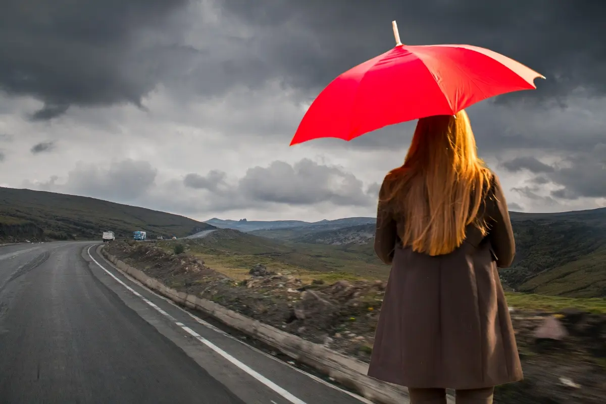 Día nublado en la carretera y una mujer con paraguas. Foto: Canva