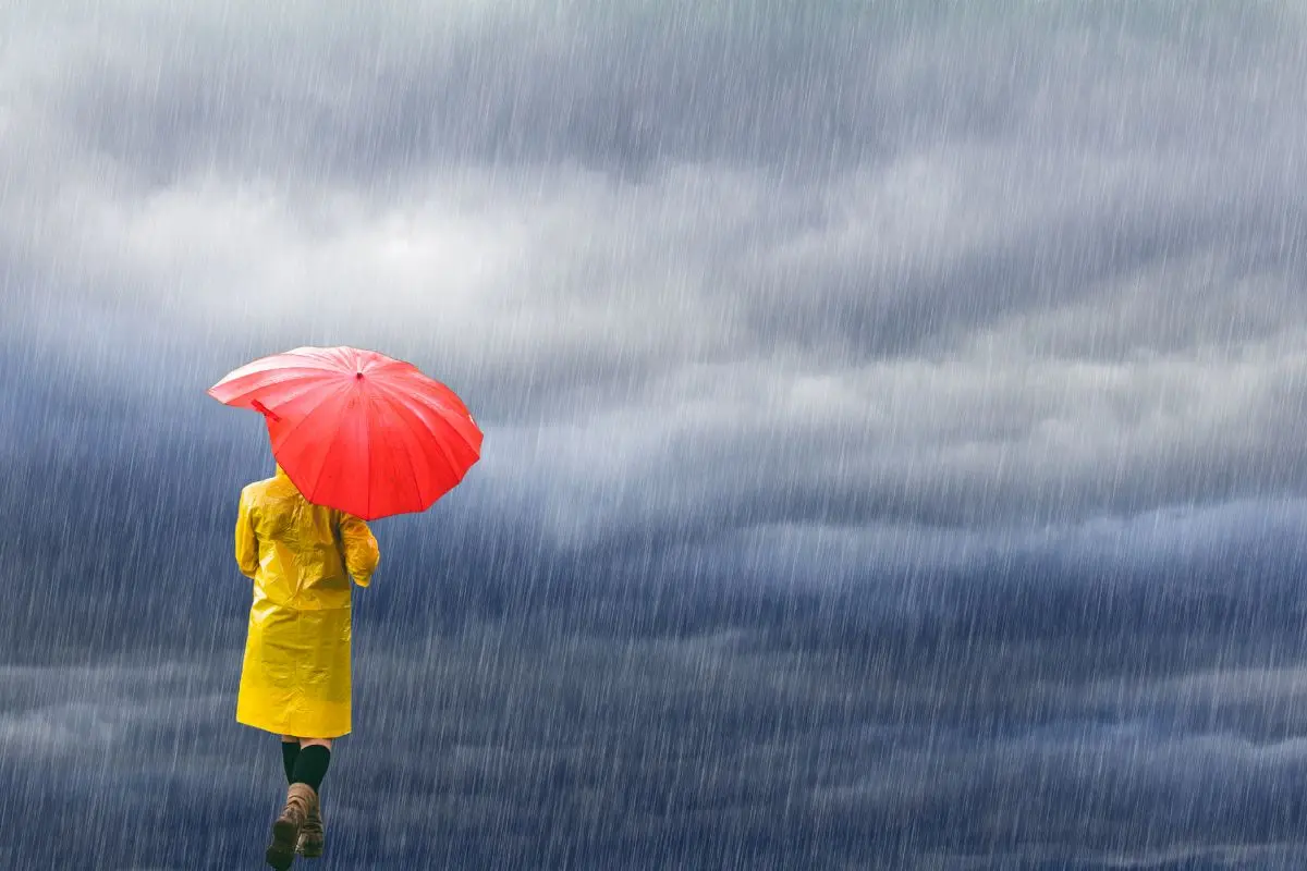 De fondo lluvia, mujer caminando con paraguas.      Foto: Canva