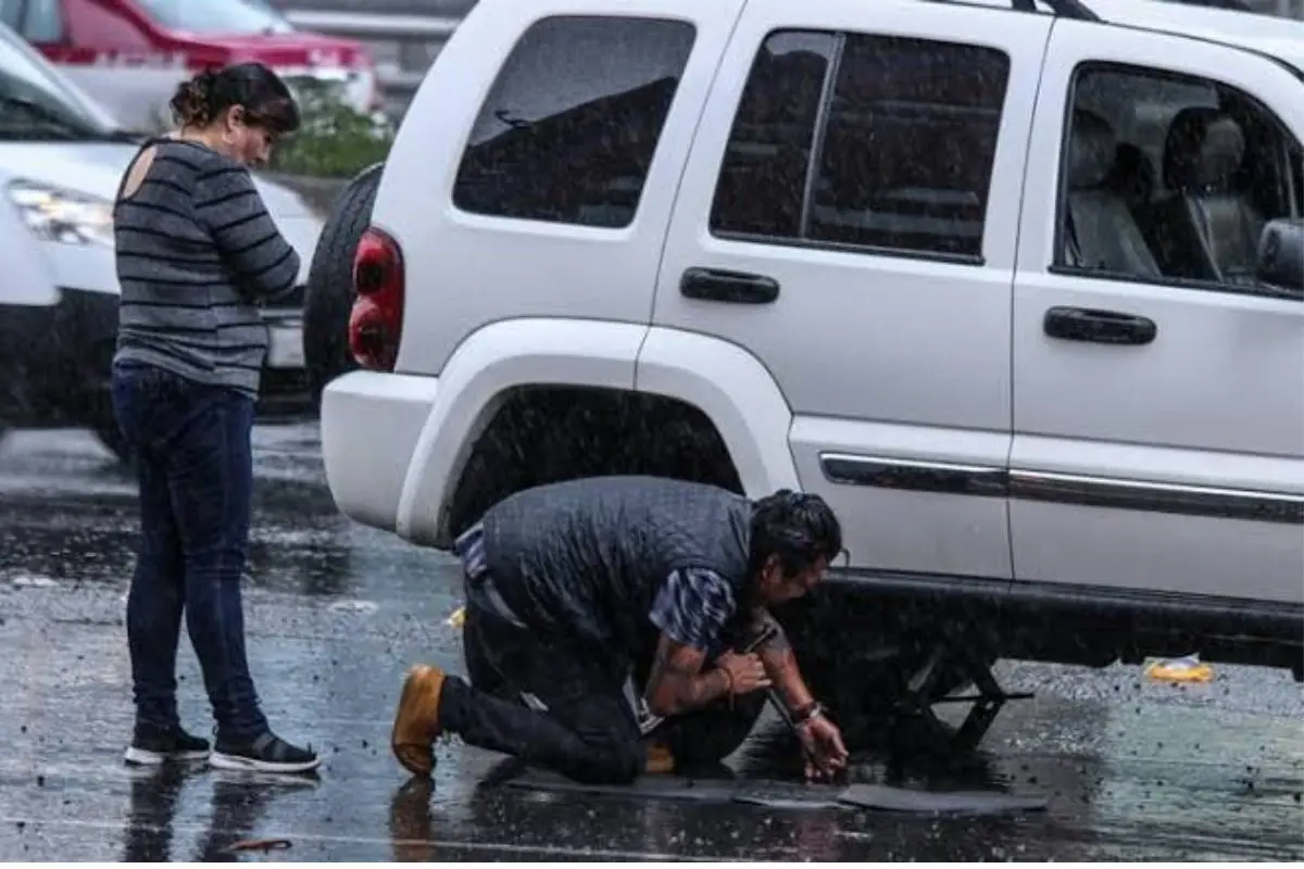 Personas revisando el daño de su auto luego de caer a un bache Foto: Canva
