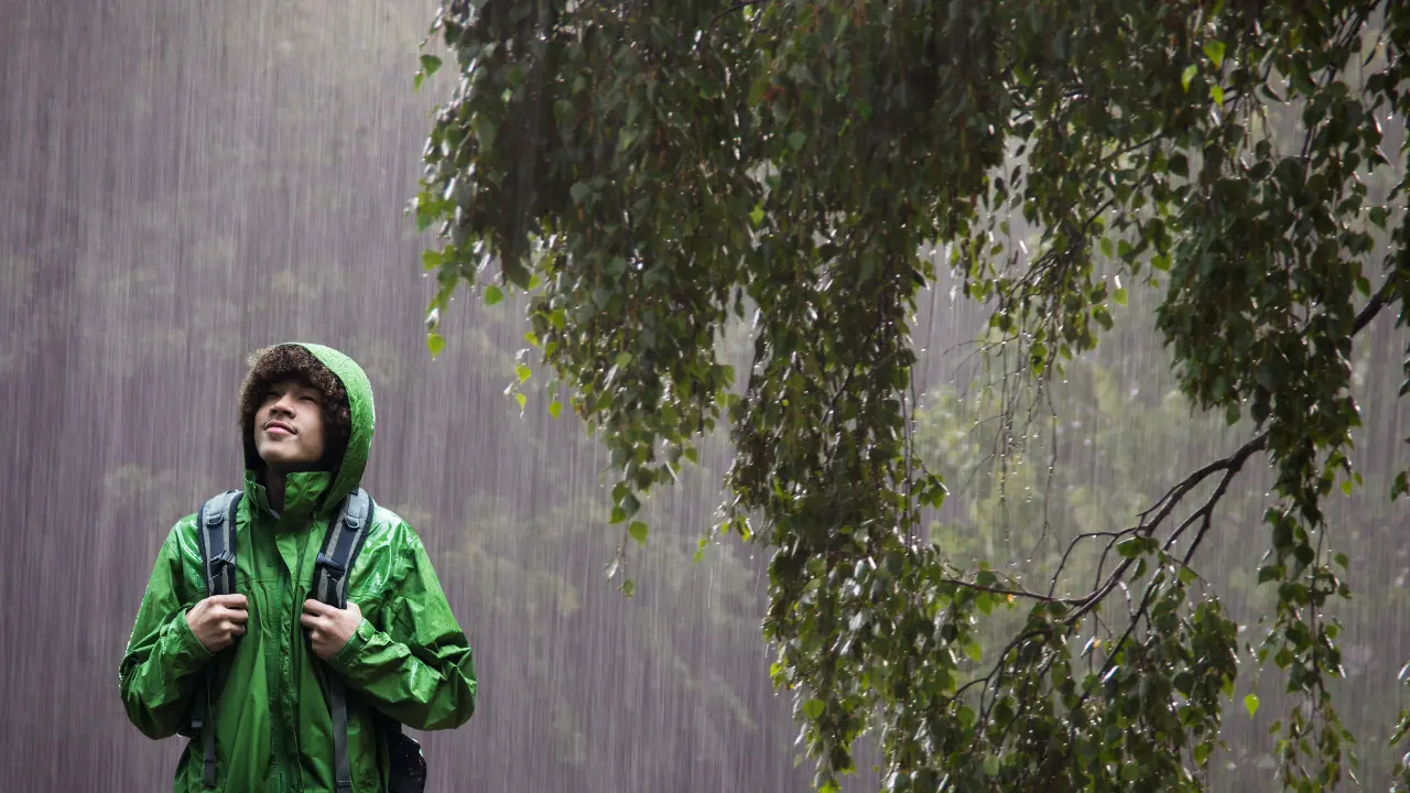 Un joven camina bajo una intensa lluvia, protegido con un impermeable. Foto: Canva