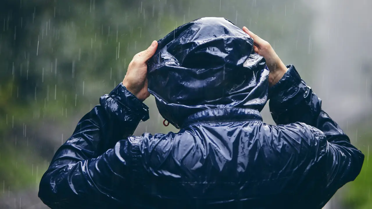 Bajo la lluvia, una persona se cubre con un impermeable negro. Foto: Canva