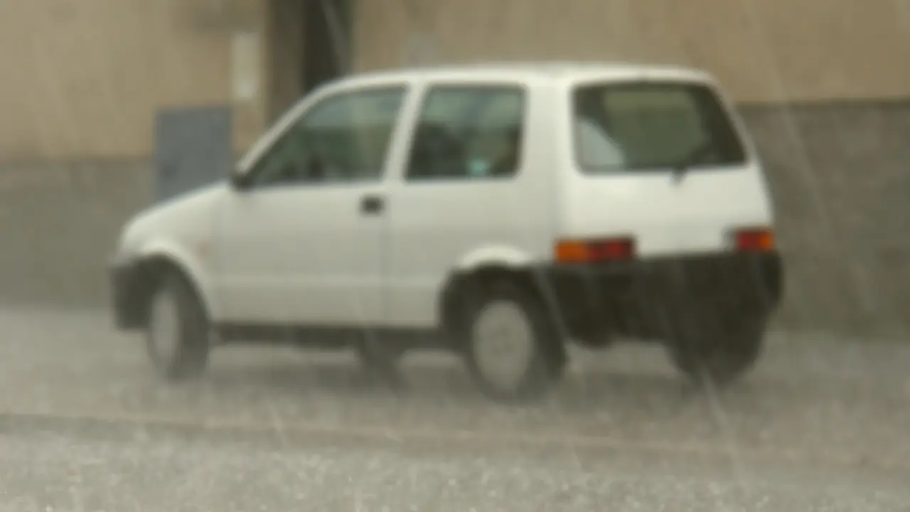 Un auto blanco en medio de una fuerte lluvia. Foto: Canva