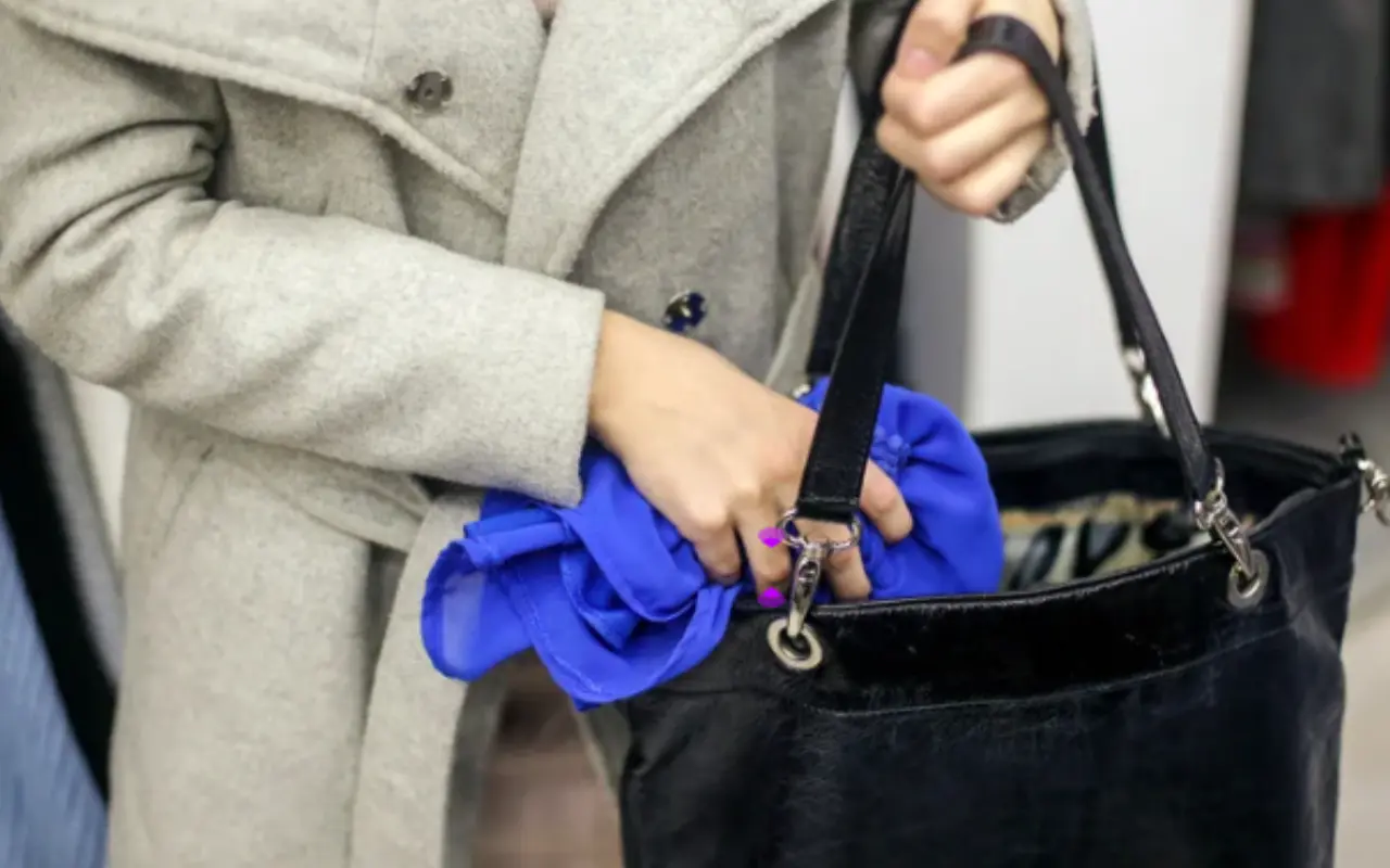 Mujer coloca discretamente una prenda de ropa en su bolso. Foto: Canva