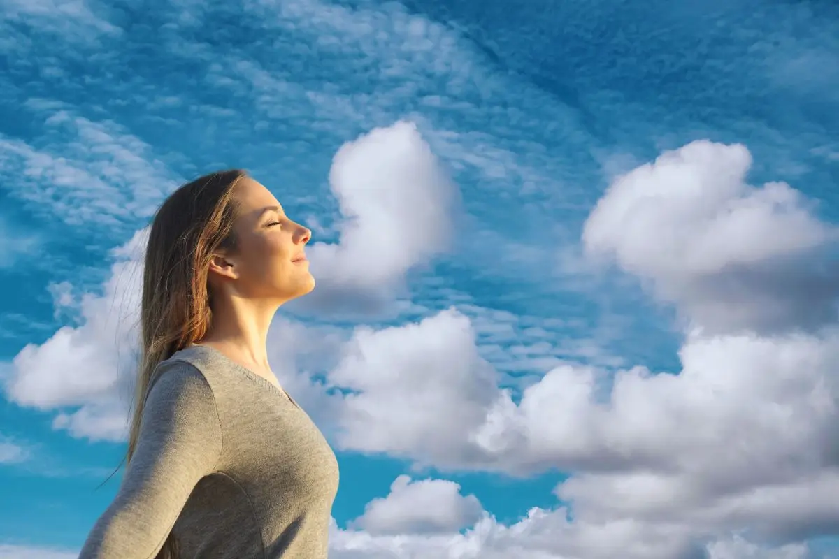 Mujer respirando con cielo de fondo Foto: Canva