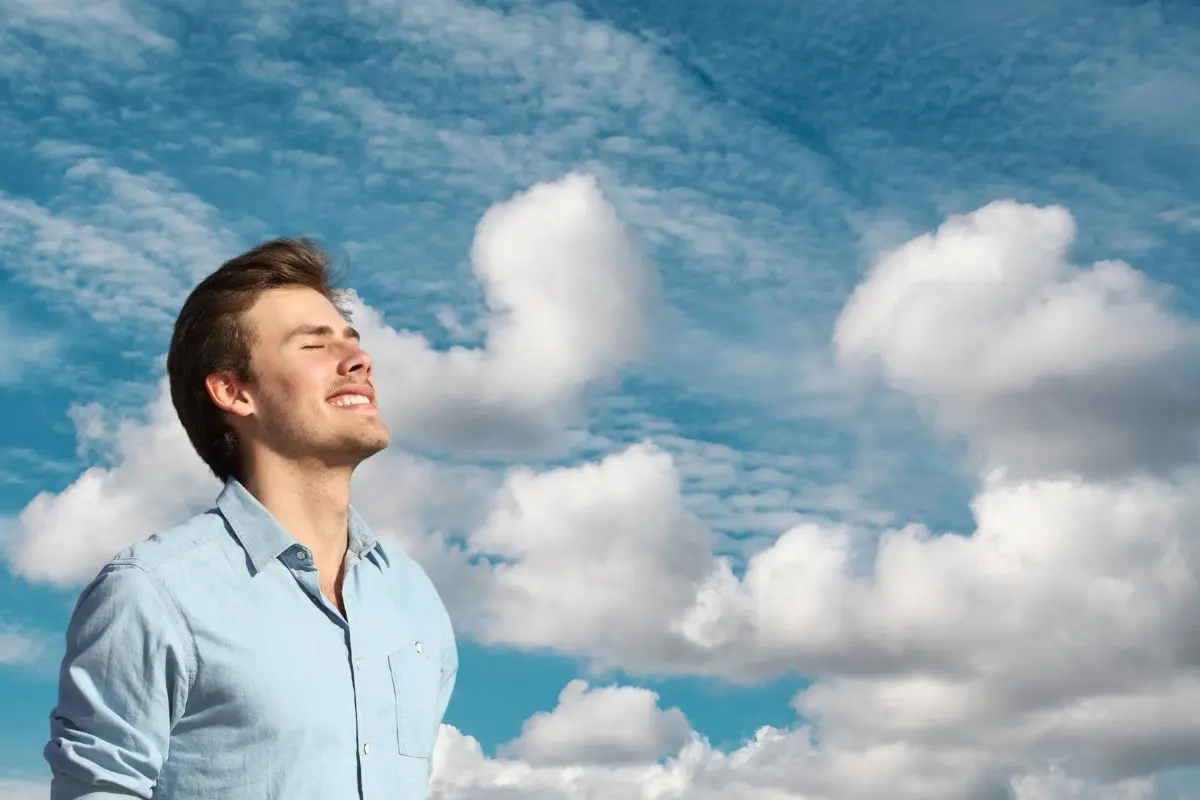 Hombre respirando y de fondo el cielo con nubes Foto: Canva