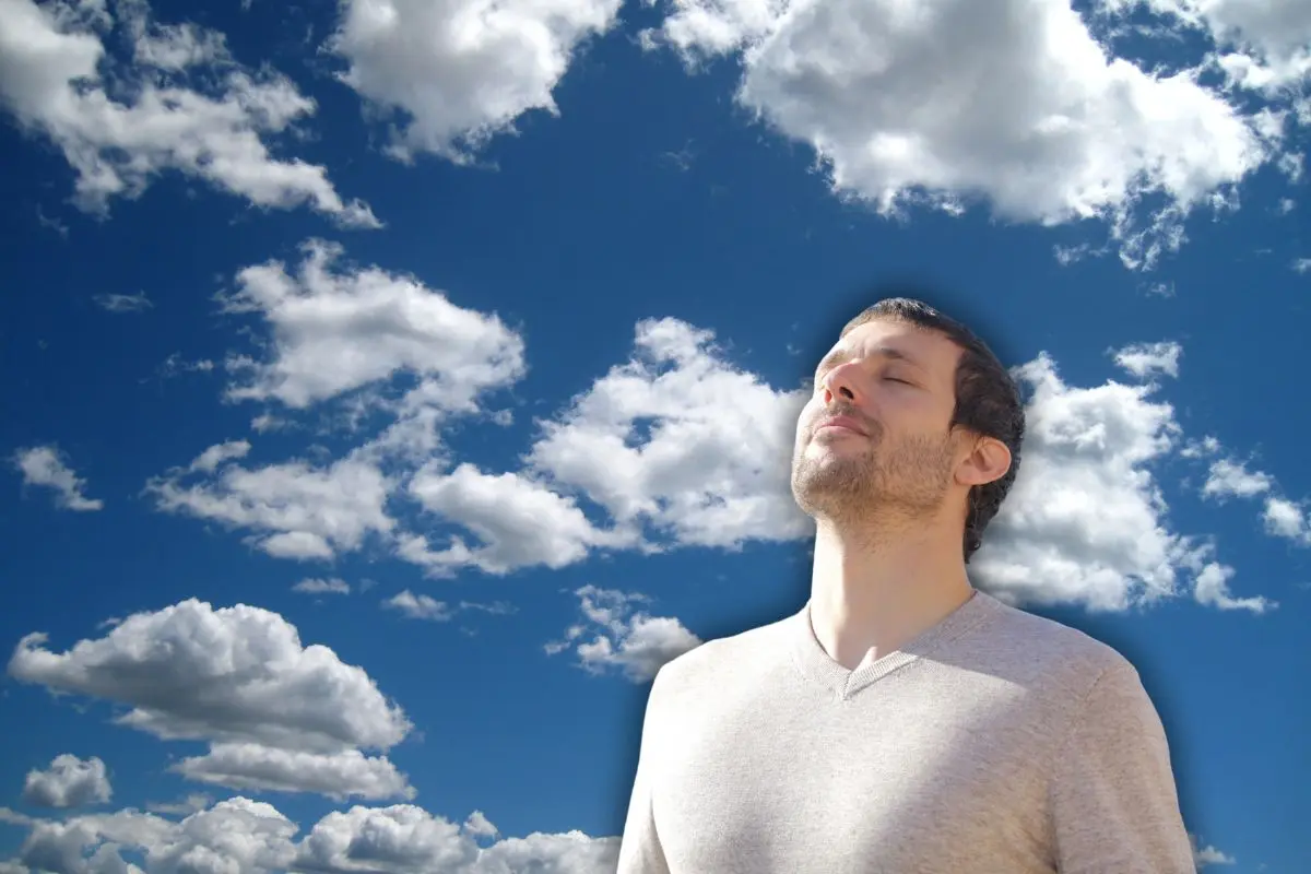 Hombre con ojos cerrados y de fondo un cielo con nubes Foto: Canva
