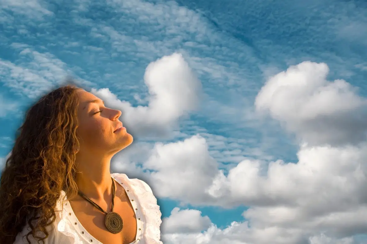 Mujer respirando y de fondo un cielo Foto: Canva