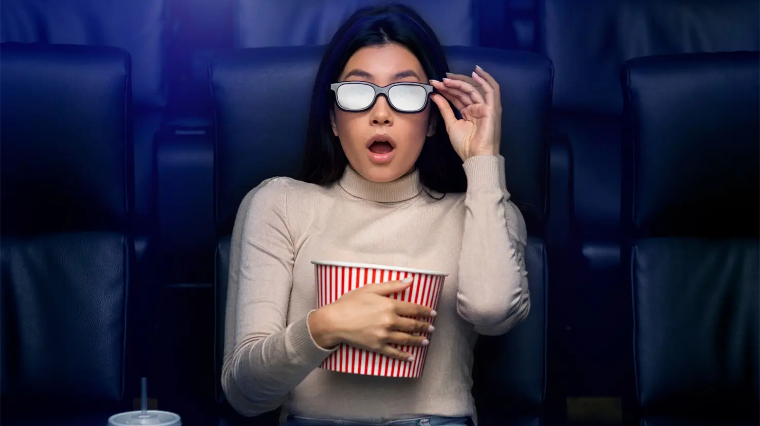 Mujer en sala de cine con palomitas en mano y lentes 3D Foto: Canva