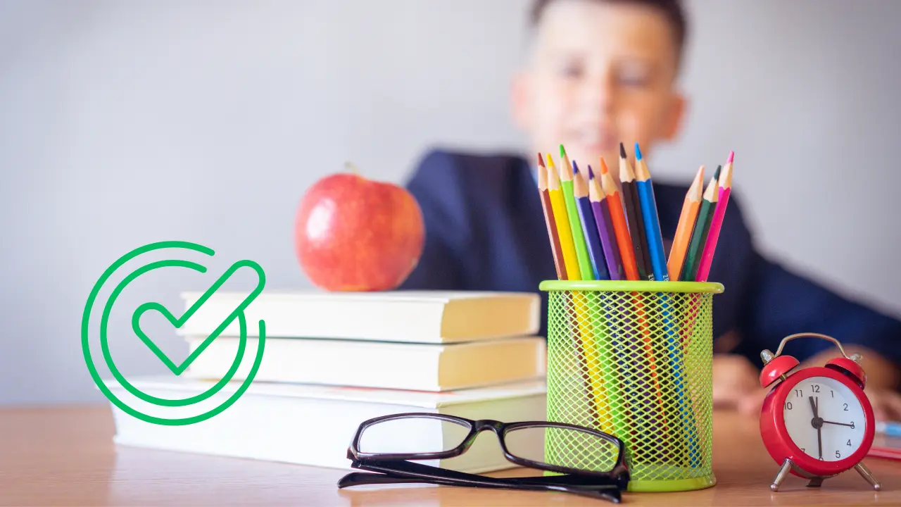 Alumno en mesa escolar con lapicero, reloj, libros, manzana y lentes| Canva Pro