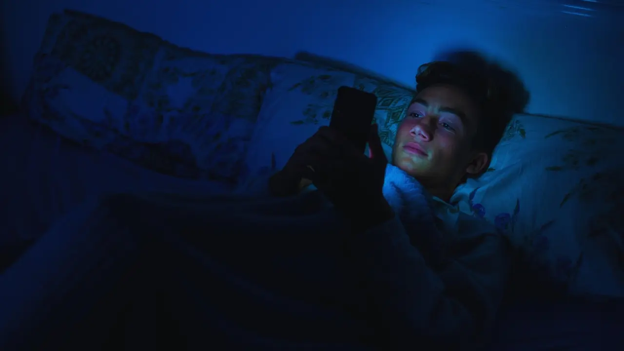 Un joven acostado y con celular. Foto: Canva