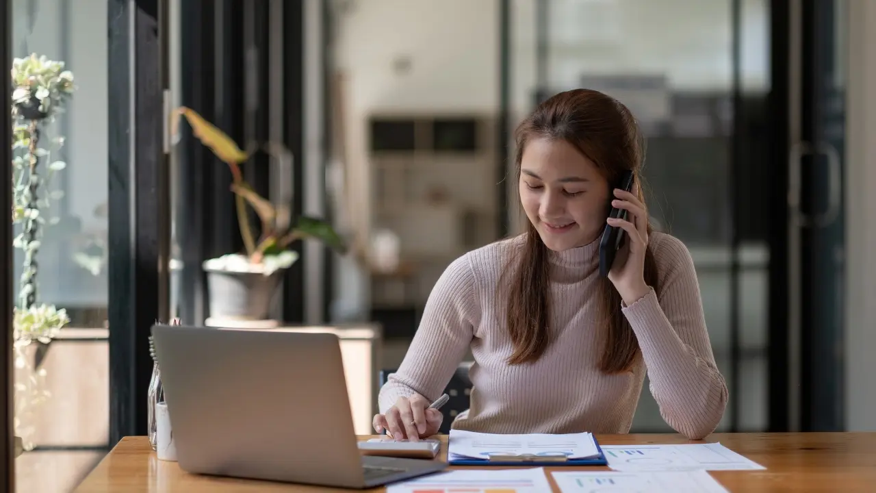 Una joven con su computadora y usando un celular. Foto: Canva