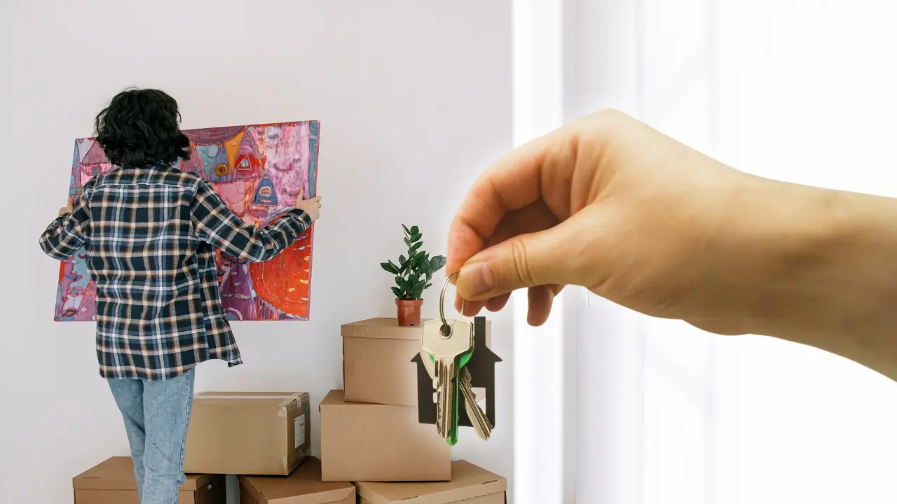 Una mujer en una vivienda con un cuadro y unas llaves. Foto: Canva