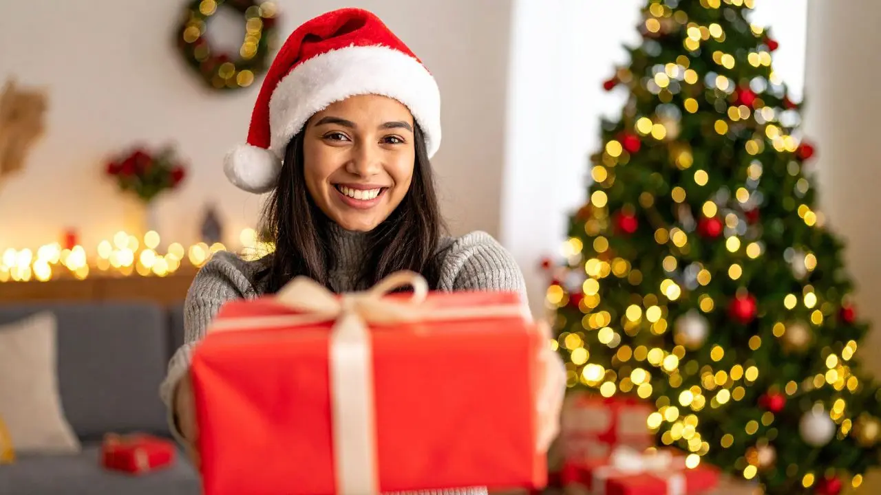 Mujer sonriendo simulando que entrega un regalo de navidad Foto: Canva