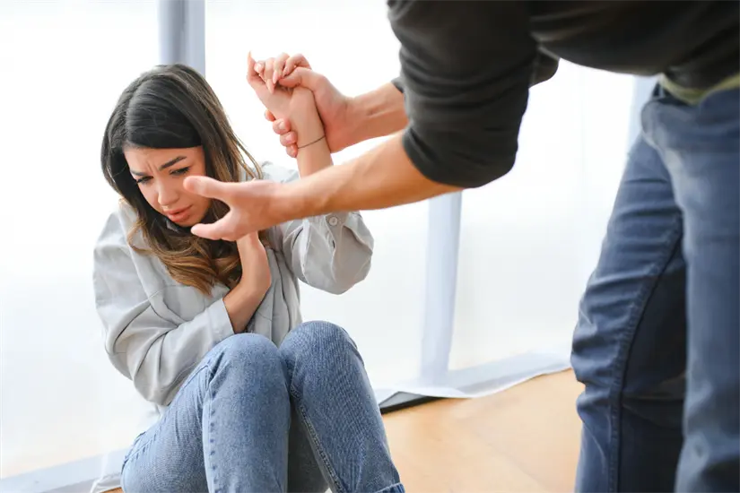 imagen recuadro Una mujer sentada en el suelo muestra miedo mientras un hombre la sujeta de la muñeca en una postura dominante. Foto: Canva