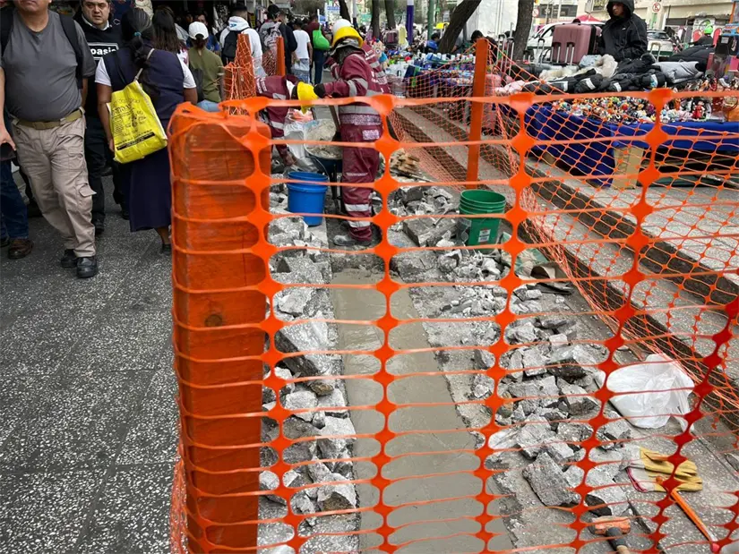 Un trabajador de la construcción en traje rojo y casco amarillo trabaja en una zanja de cemento fresco. Foto: Iván Macías