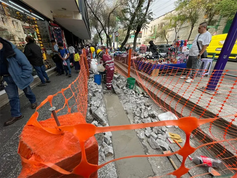 Obreros trabajan en la reparación de una acera en una calle concurrida, rodeados de barreras de seguridad naranjas. Foto: Iván Macías